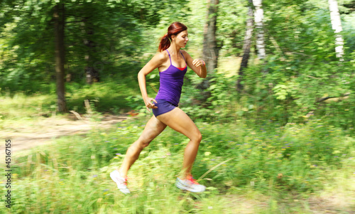 Beautiful young woman runner in a green forest. Motion blur