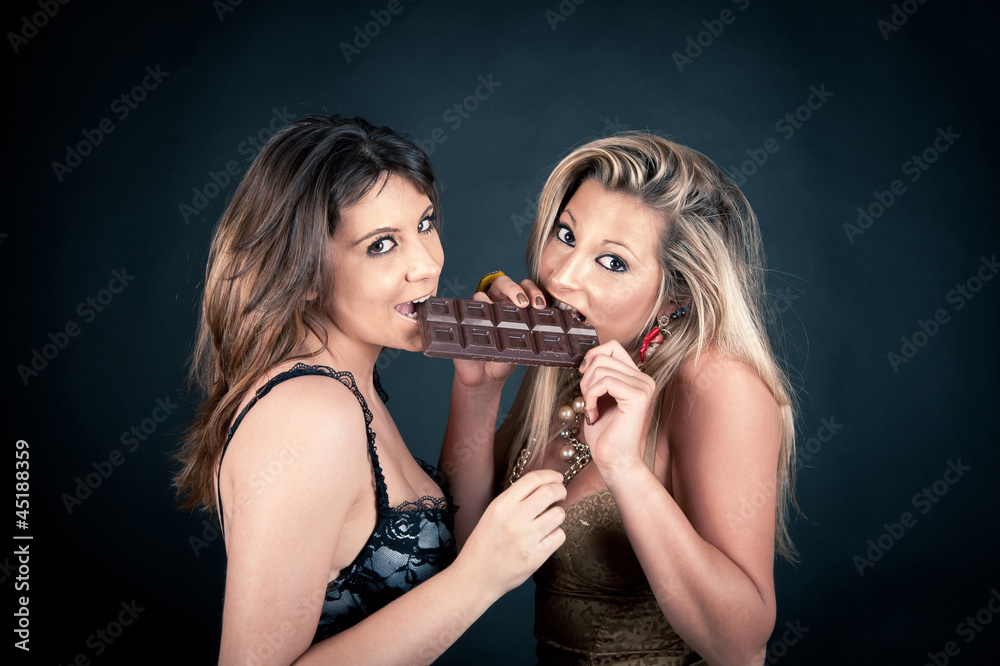 Two smiling attractive girlfriends eating chocolate bar Two smiling attractive girlfriends eating chocolate bar