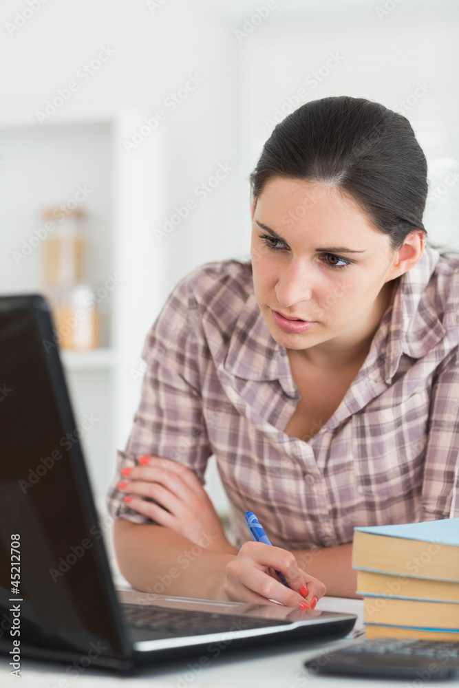 Woman writing on a notebook while looking at laptop