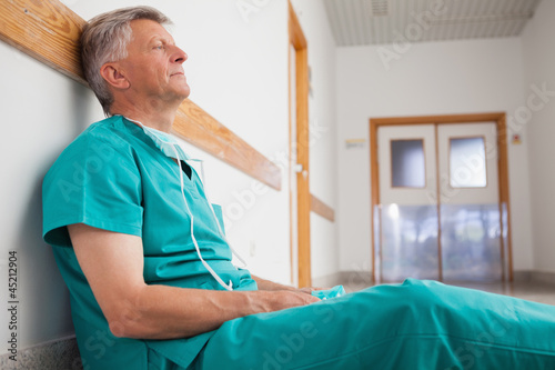 Tired surgeon is sitting on the floor in hospital corridor