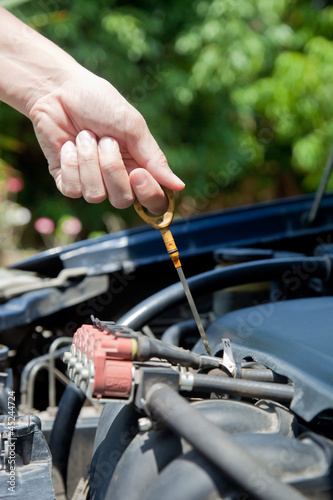 A man inspects the level of oil on a car engine dipstick.