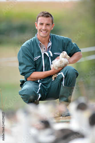 Cheerful farmer holding duck in his arms