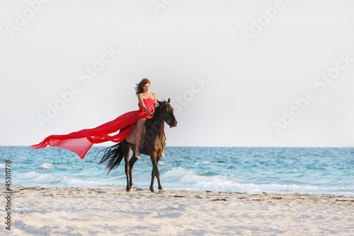 young beautiful woman in red dress riding horse on sea backgroun