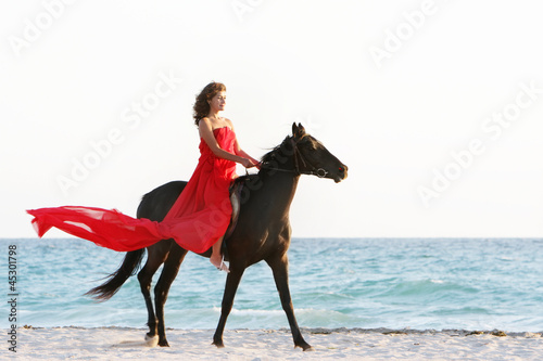 young beautiful woman in red dress riding horse on sea backgroun