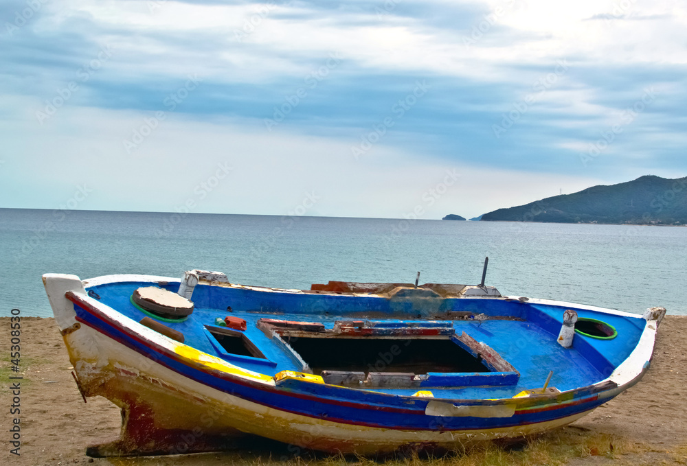 fishing boat on sand with cloudy blue sky and water
