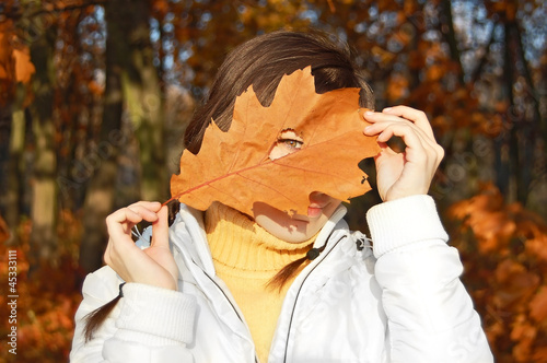 Young woman with autumn orange leaf in forest photo