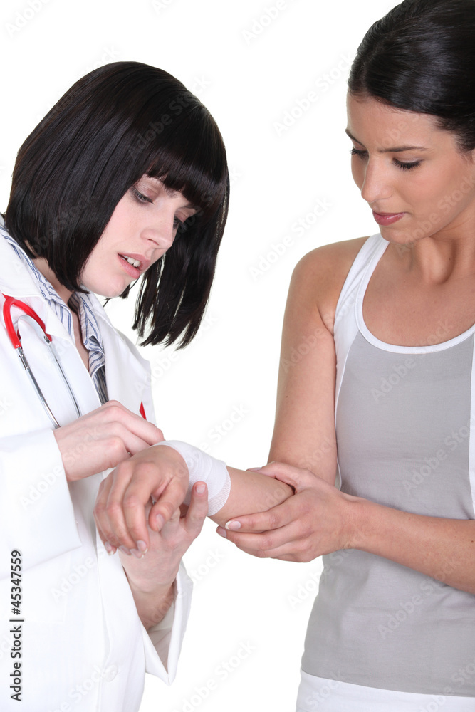 brunette nurse putting bandage on arm of female patient brunette nurse putting bandage on arm of female patient