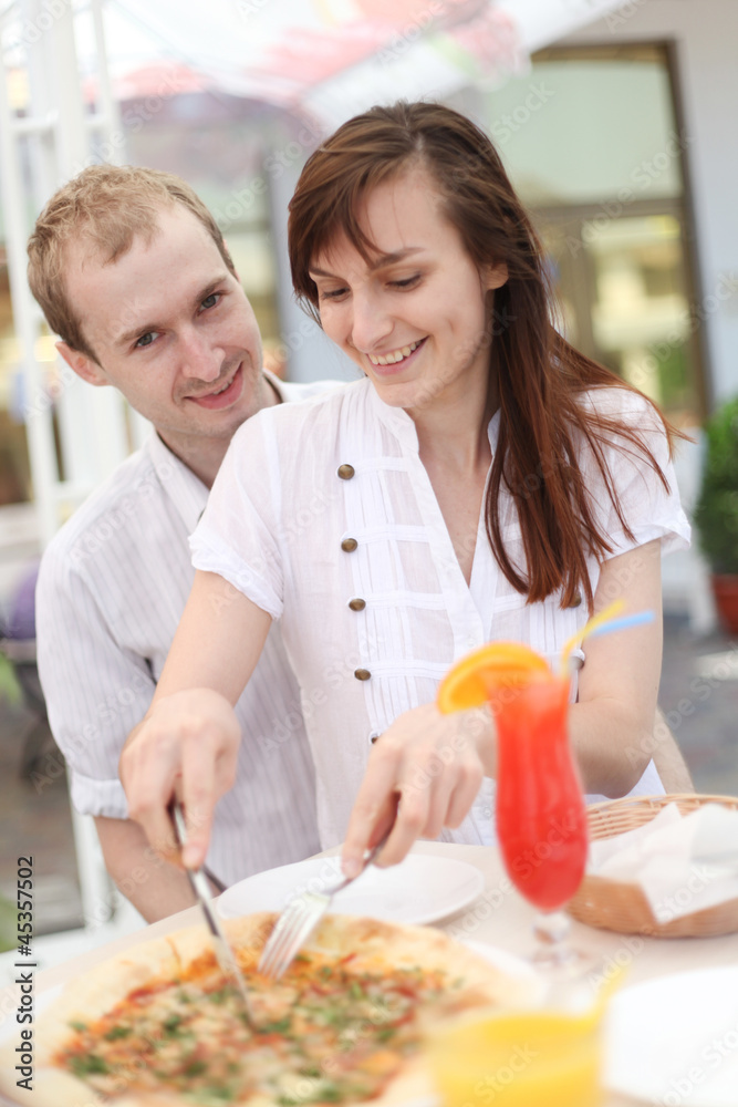 Young couple cutting pizza in cafe