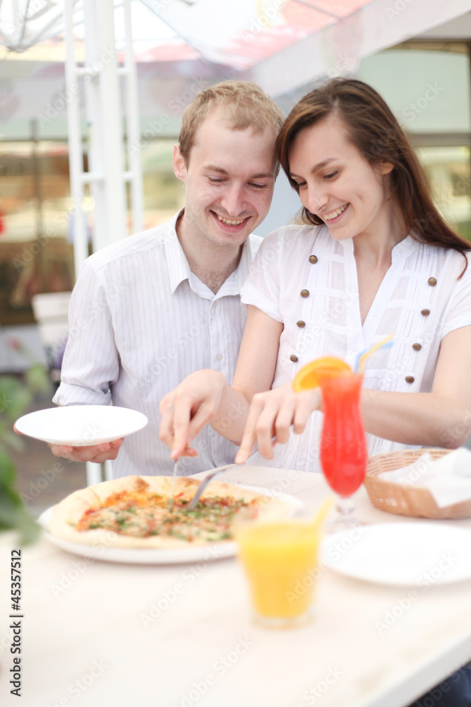 Young couple cutting pizza in cafe