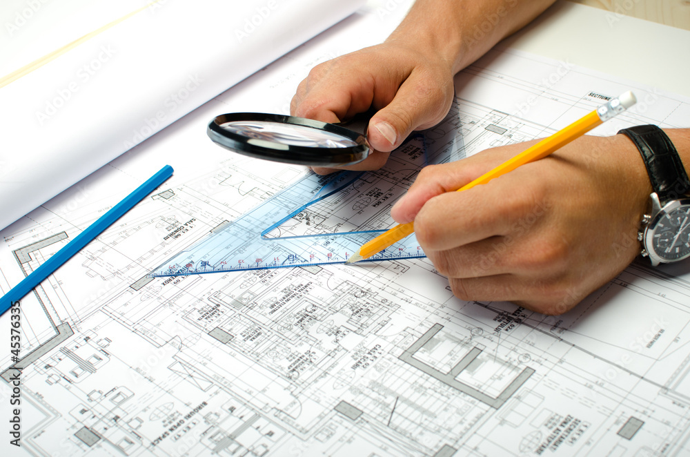 Man working with pencil and a magnifier on blueprints Man working with pencil and a magnifier on blueprints