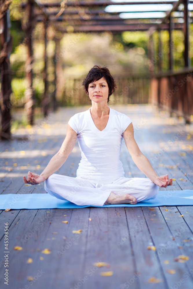 middle aged woman doing yoga meditation on deck