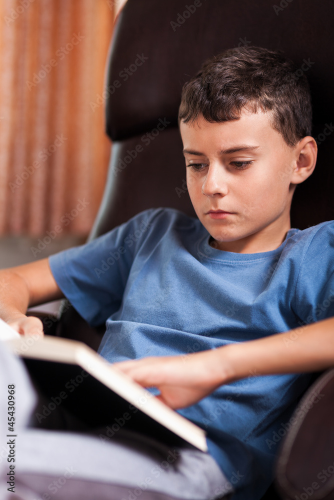 Child reading a book, sitting in an armchair