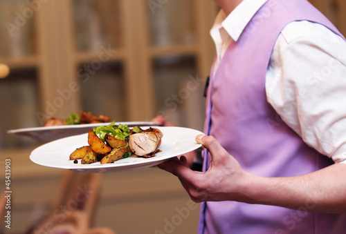 Waiter carrying two plate with meat and baked potato