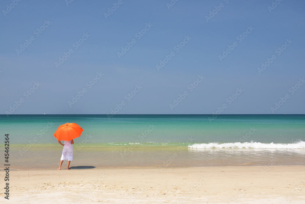 Girl with an orange umbrella on the sandy beach