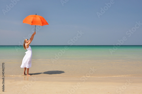 Girl with an orange umbrella on the sandy beach