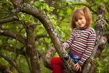 Little girl posing sitting on a tree in the garden.
