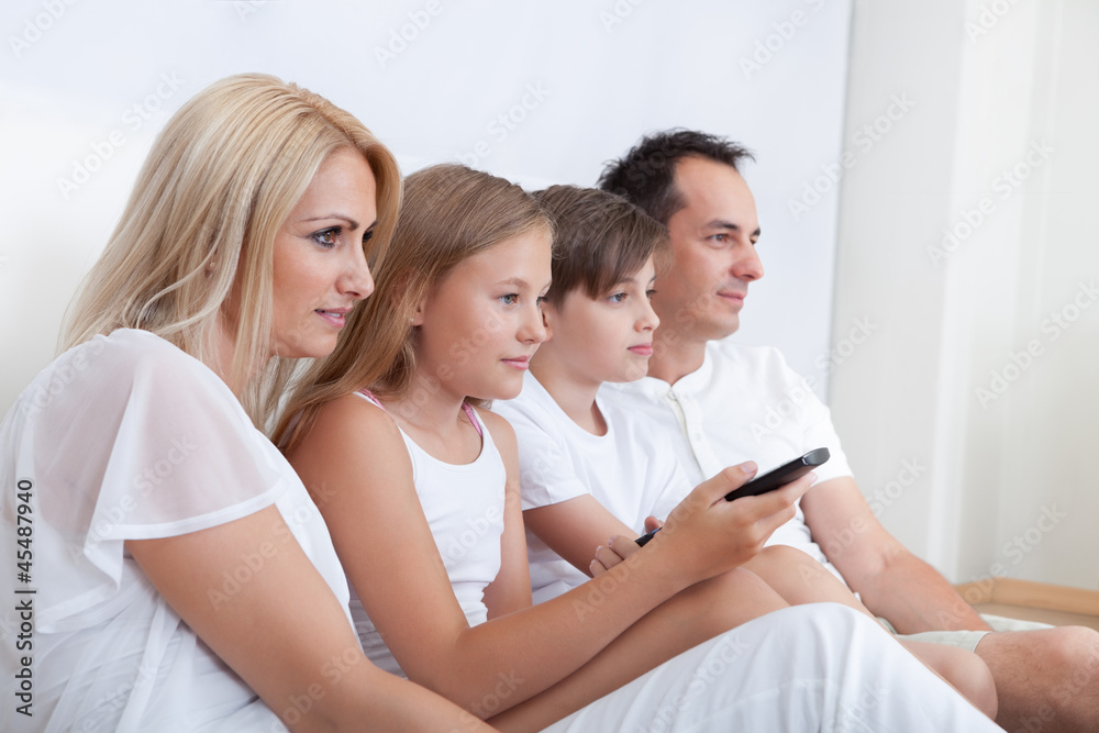 A Happy Family Sitting In Bed Watching Tv