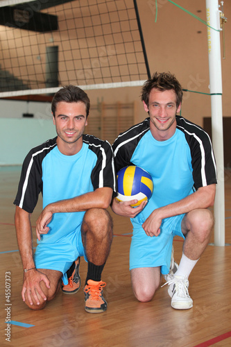 Team mates kneeling with volley ball on indoor court