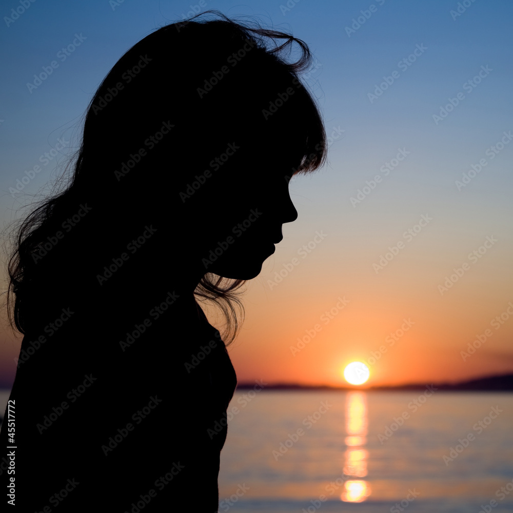 Silhouette of a little girl with sea sunset on a background