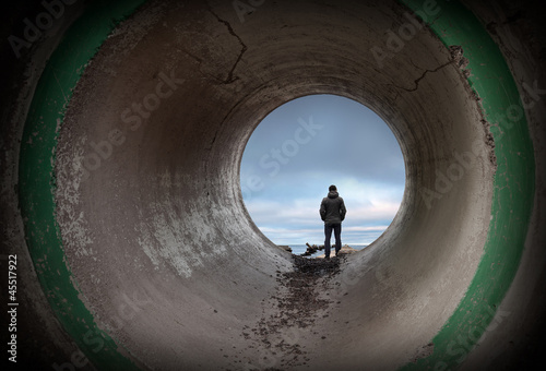 Man looks at horizon in the end of dark concrete tunnel