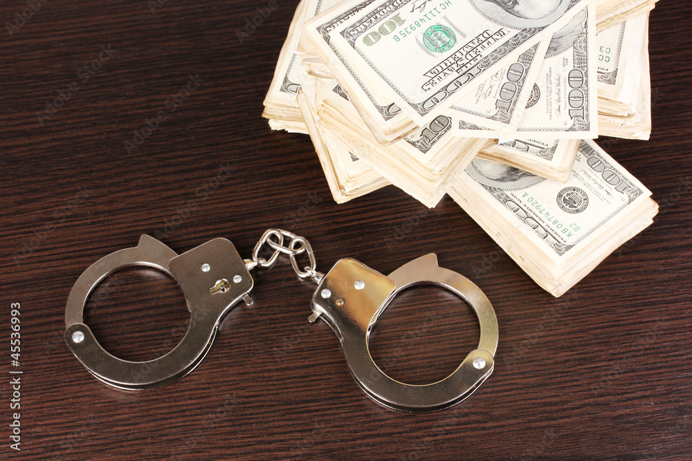 Handcuffs and packs of dollars on wooden table close-up Handcuffs and packs of dollars on wooden table close-up