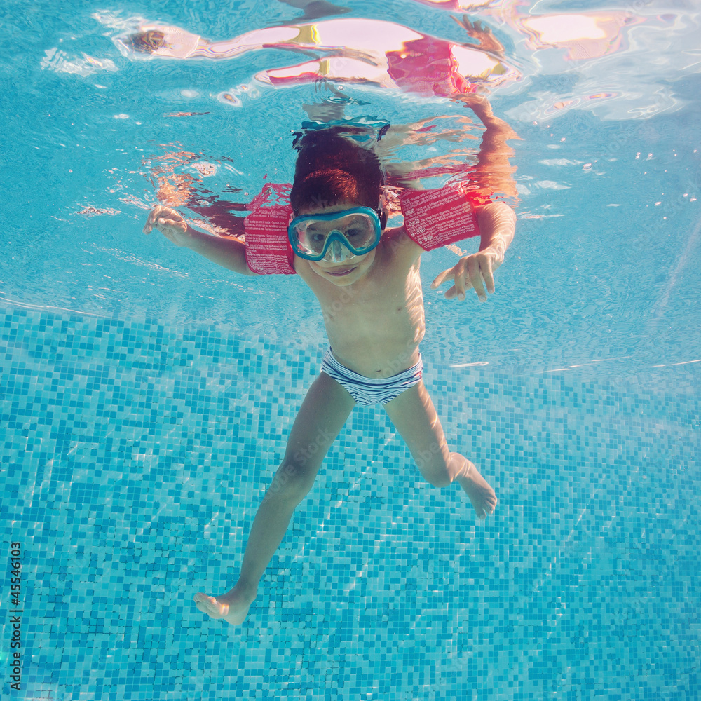 Naklejka premium Underwater little kid in swimming pool with musk and armrests.