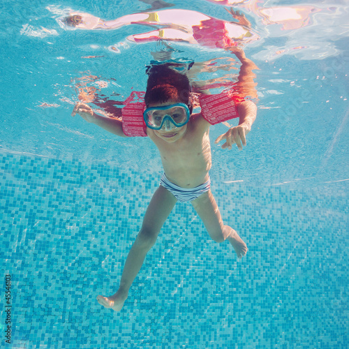 Underwater little kid in swimming pool with musk and armrests.