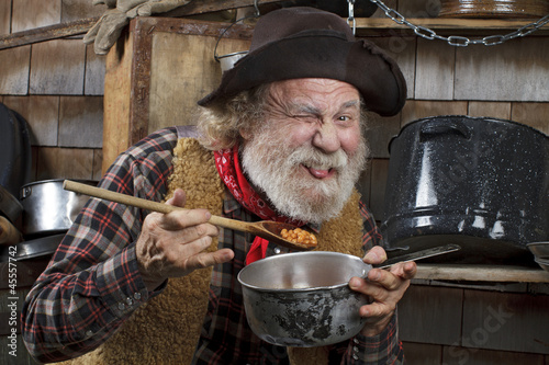Hungry old cowboy eating beans from a saucepan