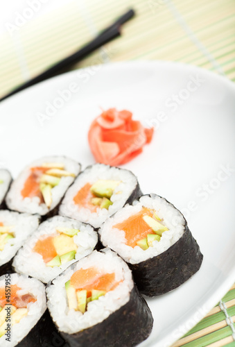 Sushi rolls on the plate with chopsticks on green mat
