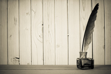 Vintage quill and inkwell on the table in front of wooden wall