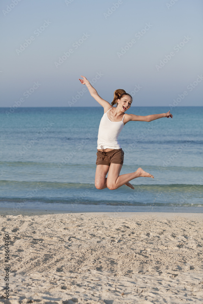 Fröhliche Frau springt lachend am Starnd Hochformat Fröhliche Frau springt lachend am Starnd Hochformat