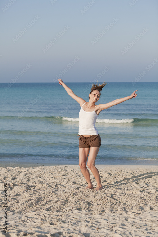 Fröhliche Frau springt lachend am Starnd Hochformat Fröhliche Frau springt lachend am Starnd Hochformat