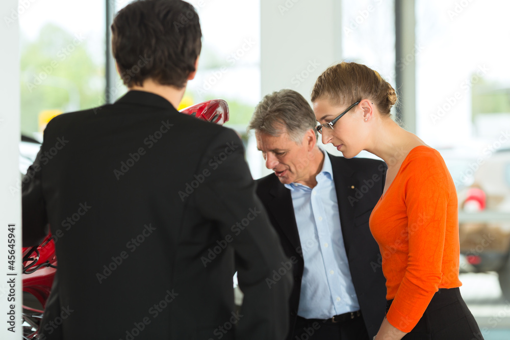 man with couple and auto in car dealership looking under hood