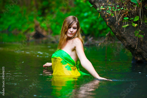 Blond young woman standing waist water in the river in green for