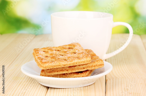 Cup of tea and cookies on wooden table on bright background