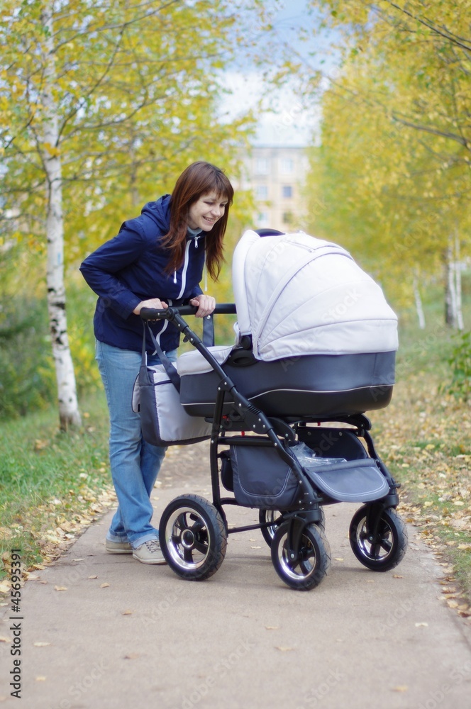 The young woman walks in autumn park with a carriage The young woman walks in autumn park with a carriage