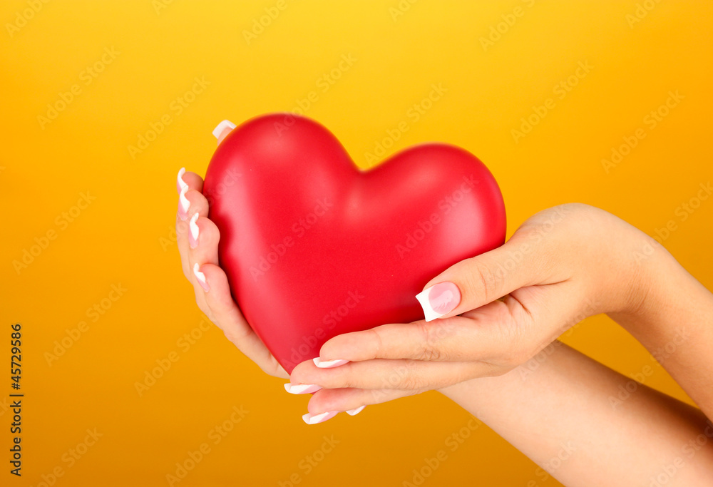 Red heart in woman's hands, on orange background close-up Red heart in woman's hands, on orange background close-up