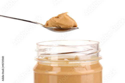 Delicious peanut butter in jar and spoon isolated on white