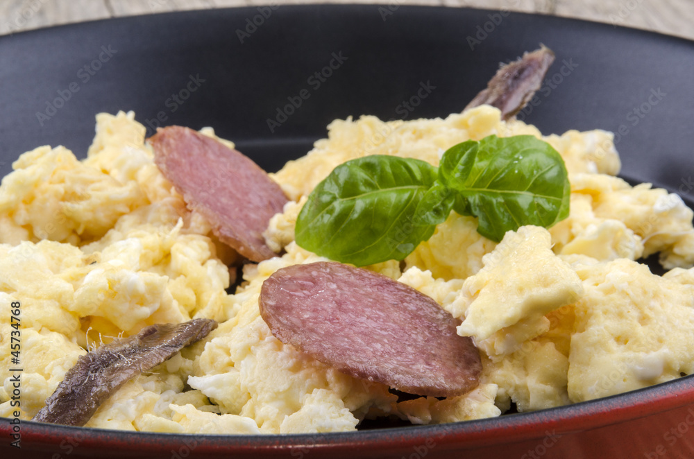 Rührei mit Salami, Sardellen und Basilikum in einer Pfanne Rührei mit Salami, Sardellen und Basilikum in einer Pfanne
