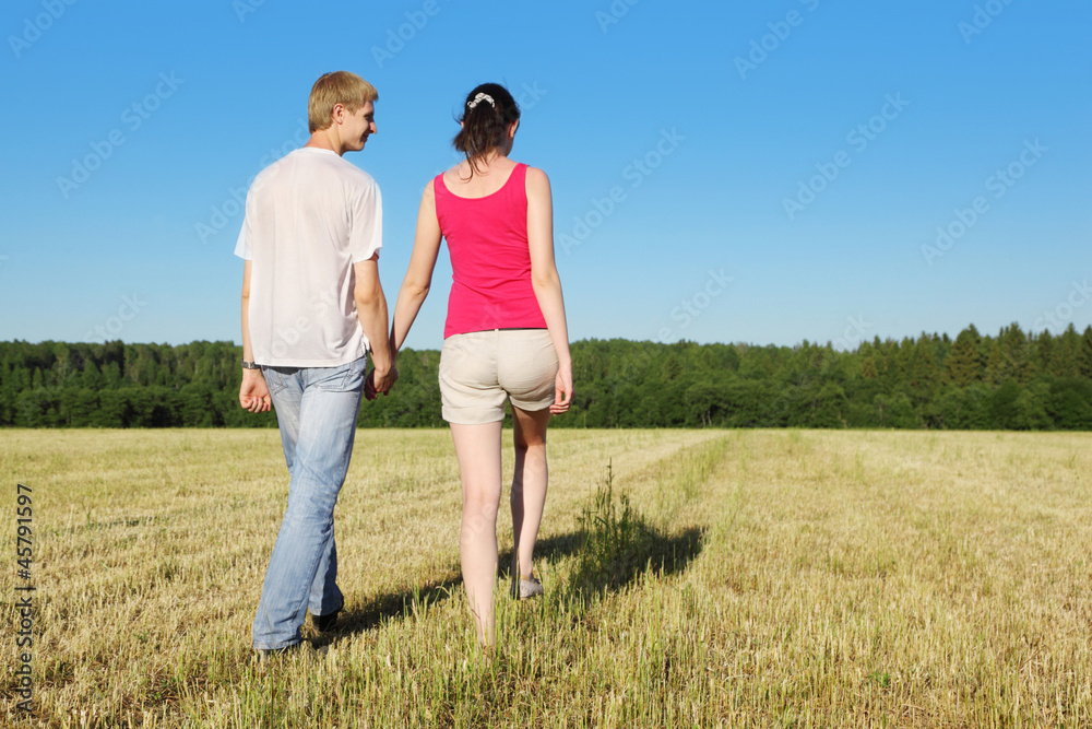 Husband, wife holding hands walking in beautiful field, back