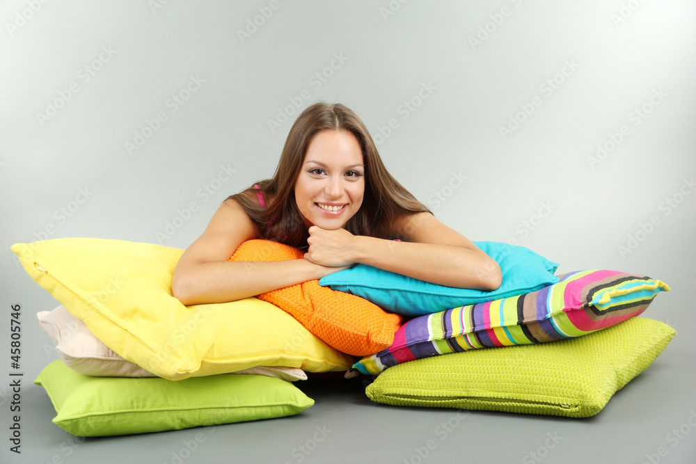 beautiful young girl with pillows on grey background