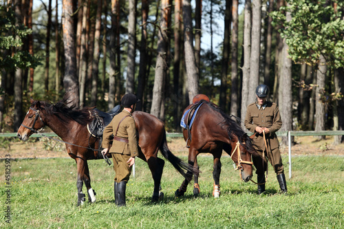 Dwóch żołnierzy z końmi na łące pod lasem. © Stanisław Błachowicz