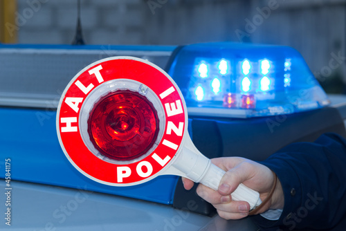 Polizist hält Polizeikelle vor Polizeiauto photo