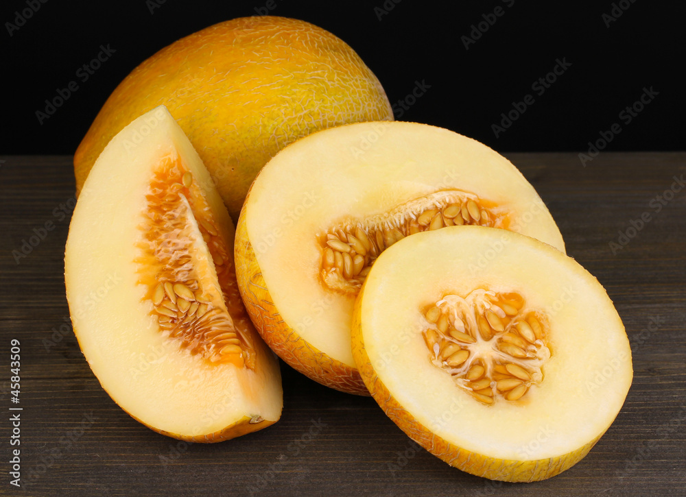 Cut ripe melons on wooden table on black background