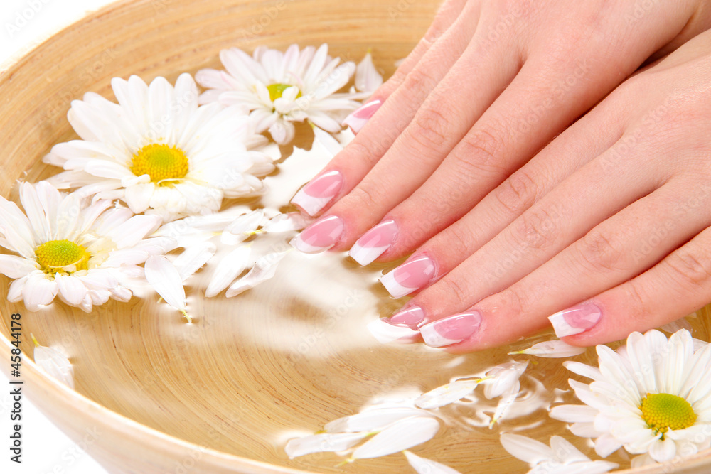 Woman hands with french manicure and flowers in bamboo bowl