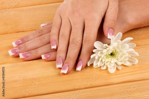 Woman hands with french manicure and flower on wooden