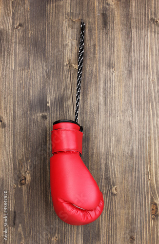 Red boxing glove hanging on wooden background
