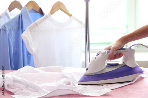 Woman hand ironing a shirt, on cloth background