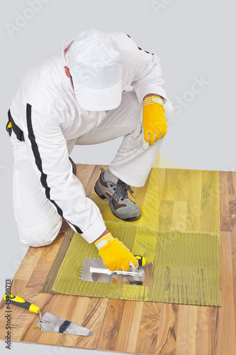 Worker applies tile adhesive on wooden floor with reinforcement