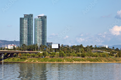 Two modern buildings and green park over river